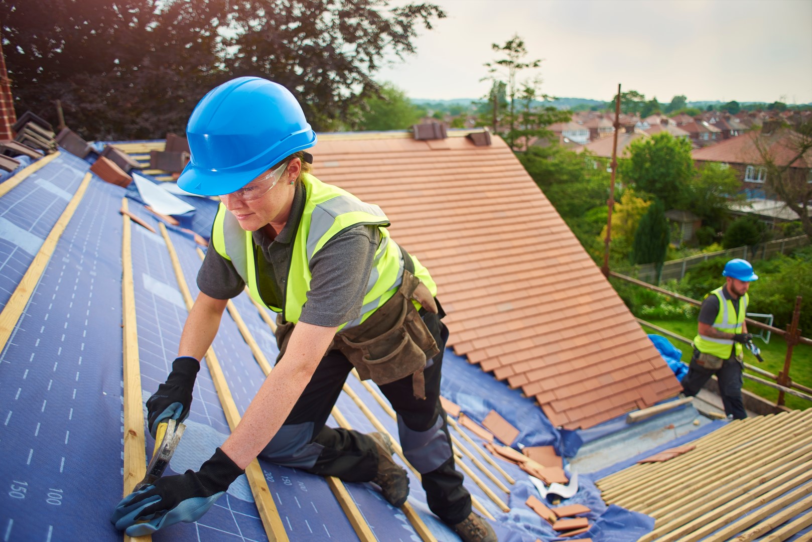 a female roofer nails on the roof tiles with her colleague