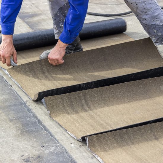 Insulation worker cutting insulation bitumen material rolls, insulation tar material over concrete slabs to keep water out.